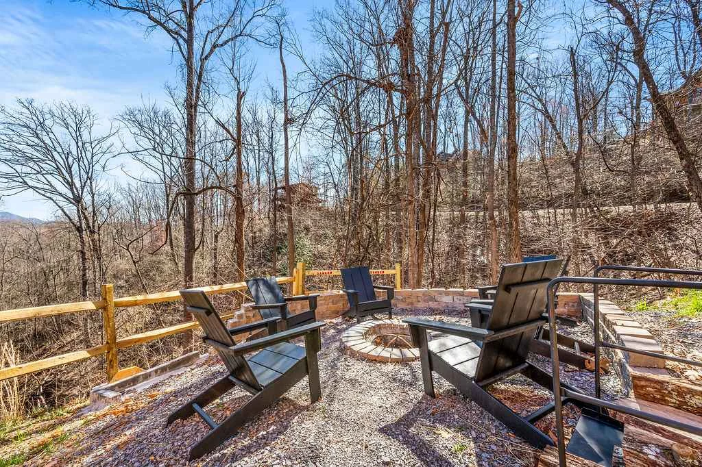 Adirondack chairs around a fire pit beside the woods